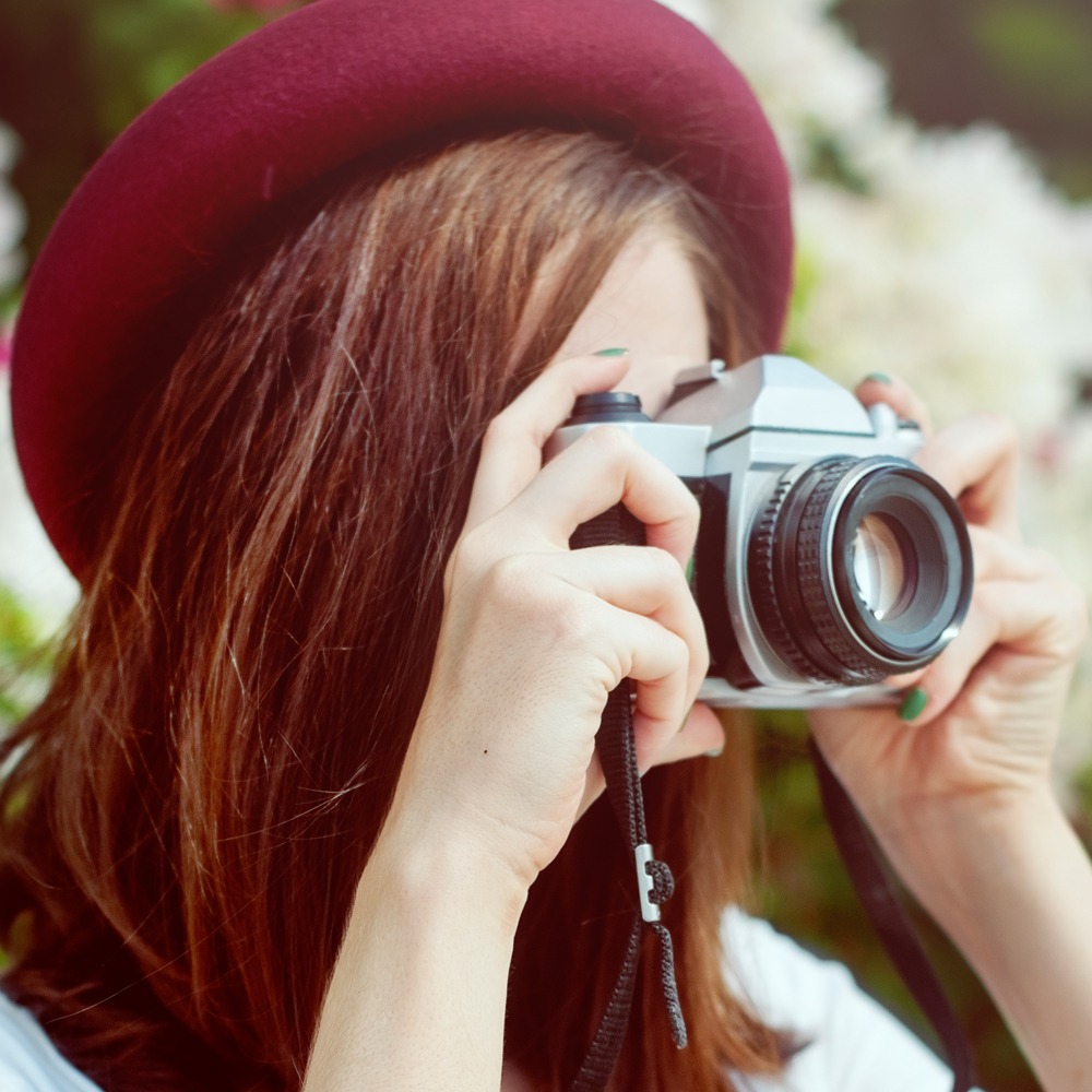 Female photographer taking a picture, wearing a burgundy hat and with brunette hair